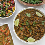 Assorted dishes including, Coconut Lemongrass Curry Chicken garnish with lime wedges and cilantro and Coconut Lemongrass Curry Shrimp, green beans,  Coconut Lemongrass Curry Blends and various salads on a white surface.