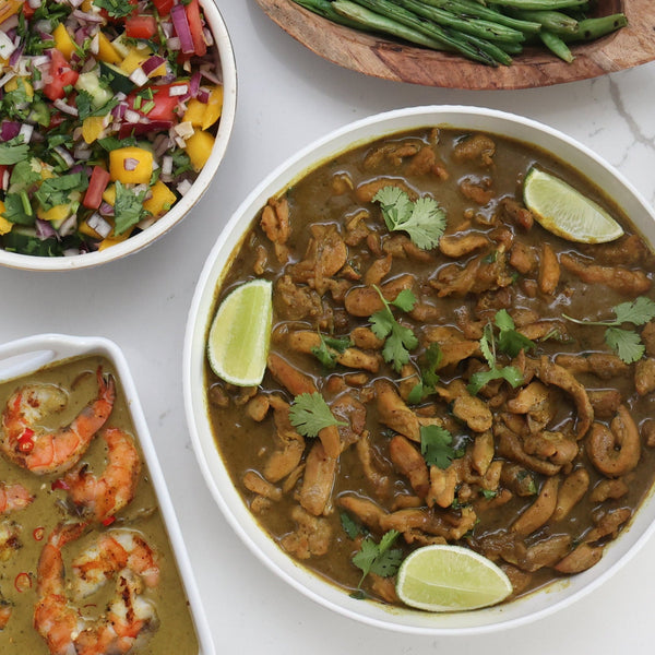 Assorted dishes including, Coconut Lemongrass Curry Chicken garnish with lime wedges and cilantro and Coconut Lemongrass Curry Shrimp, green beans,  Coconut Lemongrass Curry Blends and various salads on a white surface.