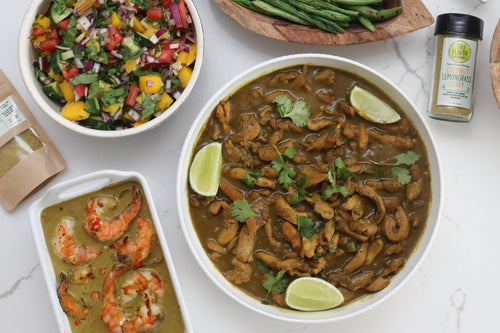 Assorted dishes including, Coconut Lemongrass Curry Chicken garnish with lime wedges and cilantro and Coconut Lemongrass Curry Shrimp, green beans,  Coconut Lemongrass Curry Blends and various salads on a white surface.