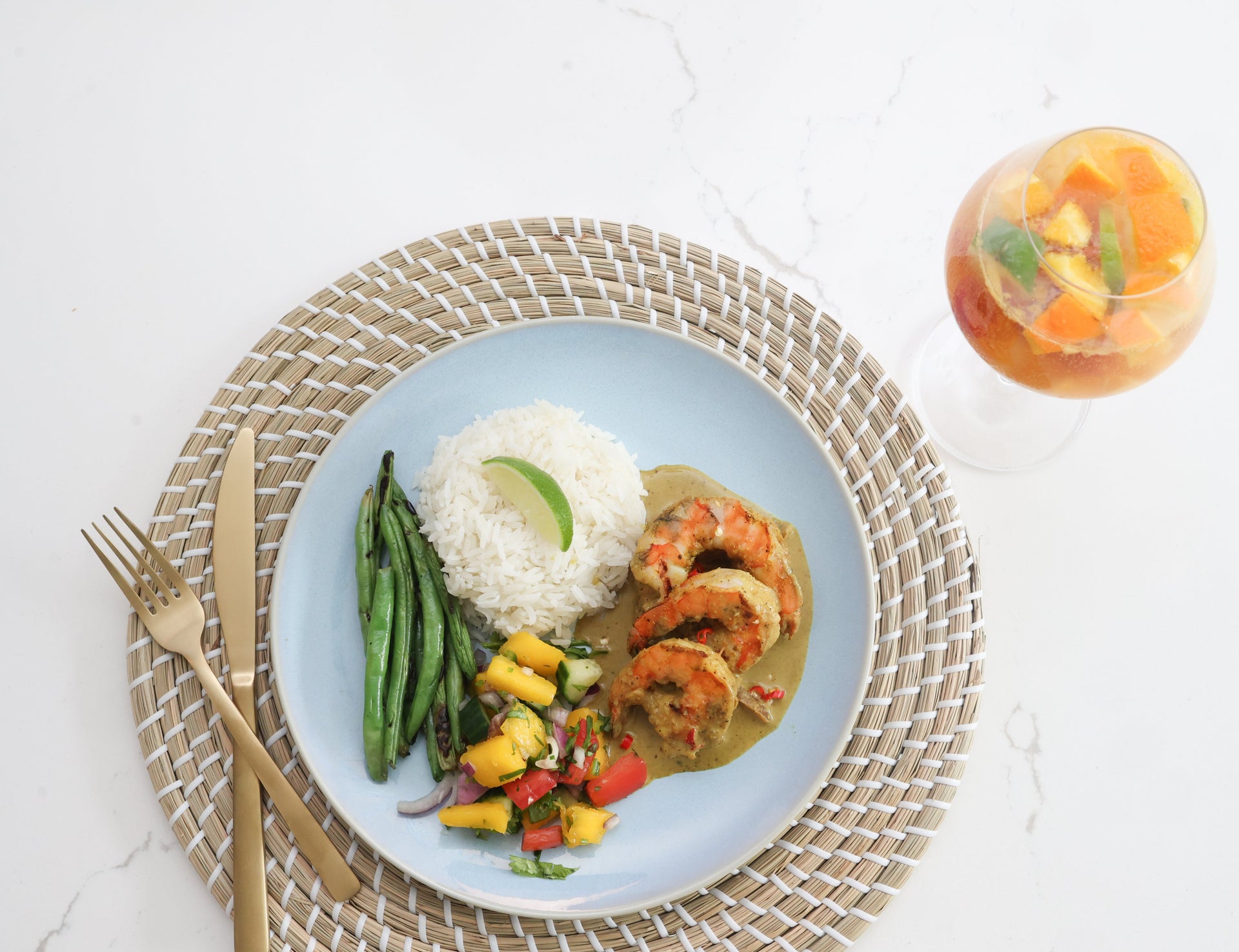  Plated meal with shrimp curry, rice, and vegetables on a white table with a glass of white wine sangria